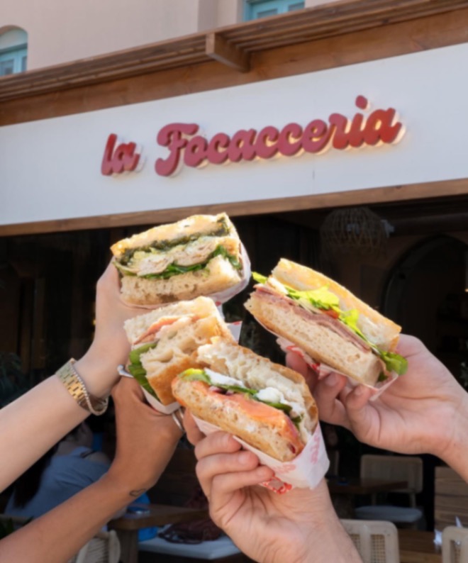 Customers holding focaccia sandwiches in front of La Focacceria's signed storefront in Downtown El Gouna
